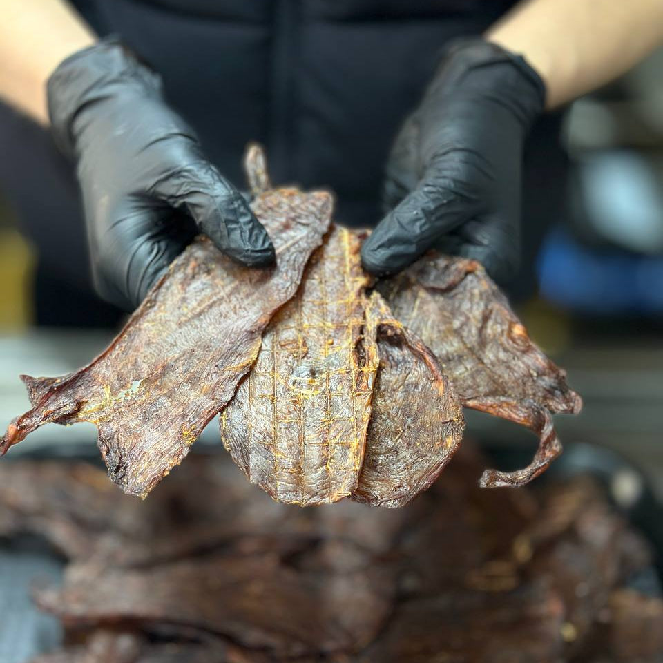 Person wearing black gloves holding dried leaf-like food items with a blurred background